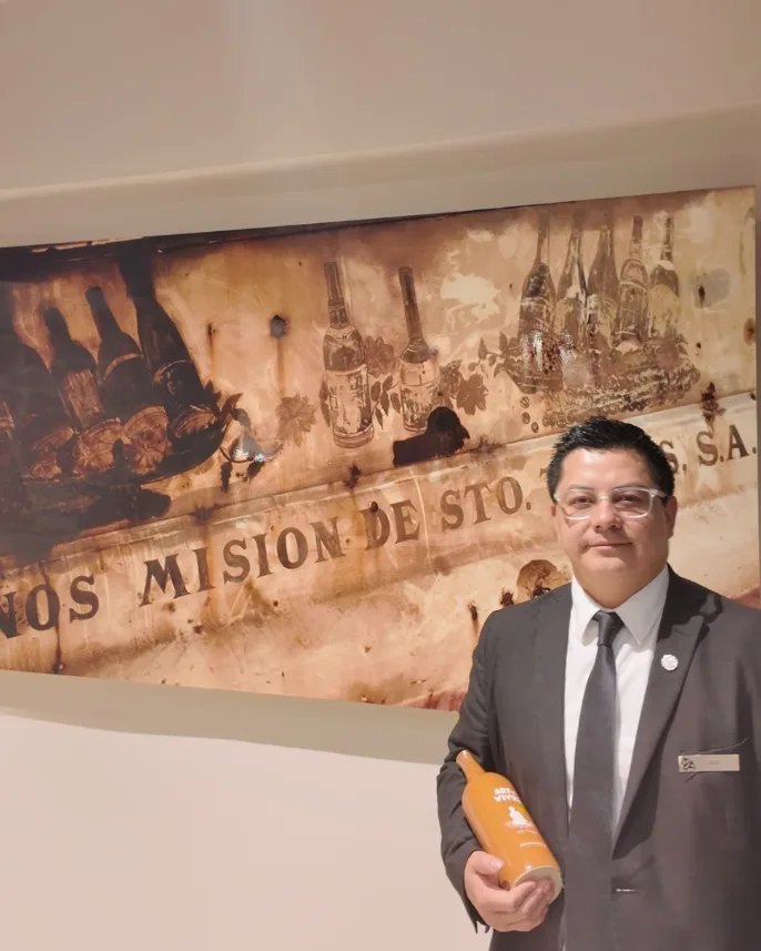 El sommelier Hugo García con una botella frente a un cuadro de botellas antiguas